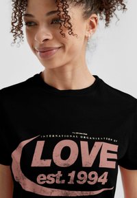 Zwarte katoen t-shirt met grote roze tekst "LOVE est. 1994" met een versleten effect, en kleinere tekst erboven in het wit.