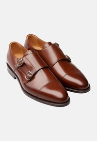 Chaussures double boucle en cuir marron avec finition brillante, bout pointu, surpiqûres contrastées et accessoires en métal argenté.