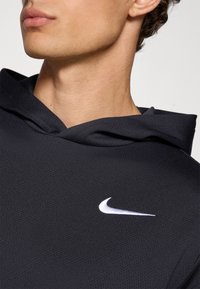 Black Nike hoodie with a textured fabric, featuring a white logo on the chest and a drawstring hood in a relaxed fit design.