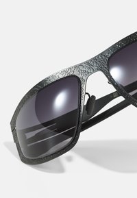 Black sunglasses with a patterned frame, dark lenses, and a sleek design. The material appears durable with a textured finish on the arms.