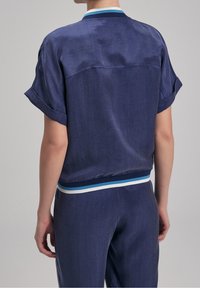 Granatowa koszula z krótkim rękawem o lekko teksturowanym materiale, z prążkowanym kołnierzem w niebieskie i białe paski oraz dopasowaną talią.