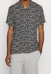 Krátký rukáv košile na knoflíky z lehkého materiálu s černým a šedým leopardím vzorem. Límec a volný střih.