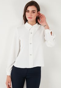 White button-up shirt with a classic collar, long sleeves, and decorative gem-like buttons at the front. Smooth, lightweight fabric.
