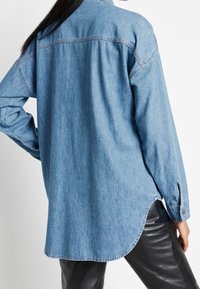 Chemise en jean bleu clair à manches longues, ourlet arrondi et poignets boutonnés. Fabriquée en tissu doux avec un col classique.