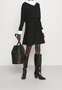 Svart långärmad topp, vit krage, utsvängd svart kjol, svarta läder stövlar upp till knäna och en svart läder bucket-väska.