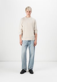 Light beige knitted sweater with ribbed cuffs, paired with light blue straight-leg jeans and black shoes, set against a plain white background.