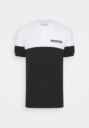 Biało-czarna koszulka polo z kołnierzykiem, krótkim rękawem oraz logo Calvin Klein Jeans na lewej górnej części piersi, w kolorze czarno-białym.