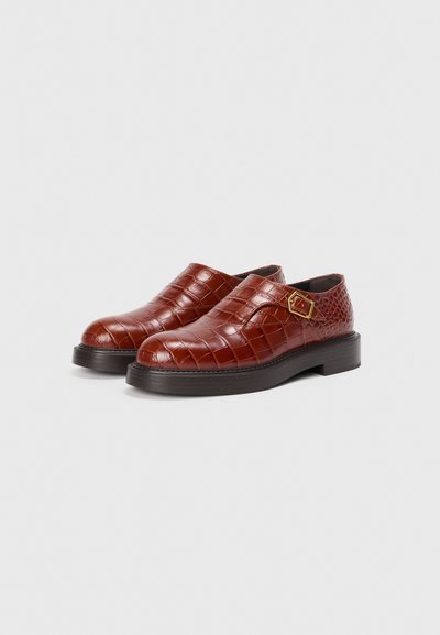 Zapatos de piel marrón con textura de cocodrilo, puntera redondeada y correa lateral con un acento dorado. Suela de goma negra para un mejor agarre.