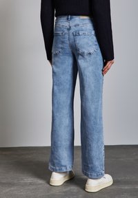 Jeans de pernera ancha de color azul claro con un lavado deslavado, que cuentan con dos bolsillos traseros y un dobladillo vuelto. Combinados con zapatillas blancas.