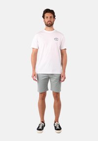 T-shirt en coton blanc avec un col rond et un petit graphique sur la poitrine, assortie à un short gris clair et des baskets noires.
