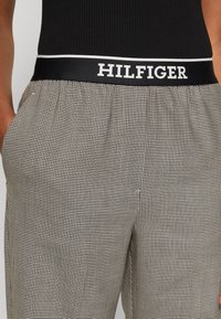 Musta-valkoiset ruudulliset housut, joissa on joustava vyötärönauha mustalla nauhalla ja valkoisin kirjaimin teksti "HILFIGER".