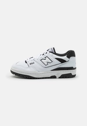 Biało-czarne buty sportowe New Balance 550 z perforowanymi bokami, czarną podeszwą zewnętrzną i detalami logo na boku oraz języku, sfotografowane na białym tle.