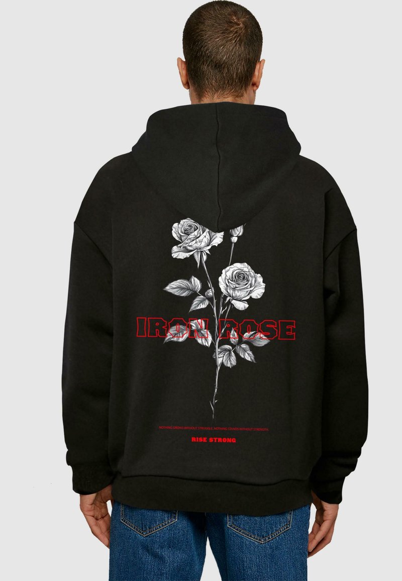 Mustika musta kapuutsiga, millel on valgete rooside lilleline graafika ja punased tähed "IRON ROSE". Sellel on suhteliselt vaba lõige ja kängu tasku.