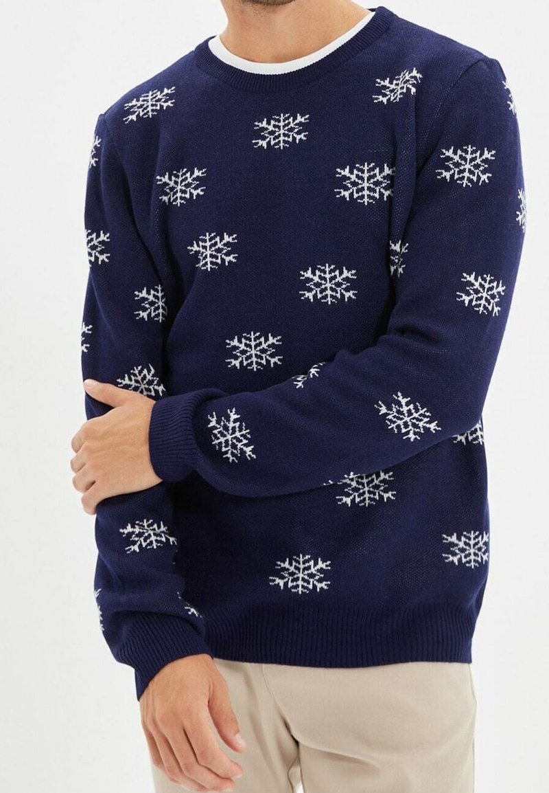 Pull en maille bleu marine avec motifs de flocons de neige blancs, col rond et poignets côtelés. Le tissu est doux avec une texture lisse.