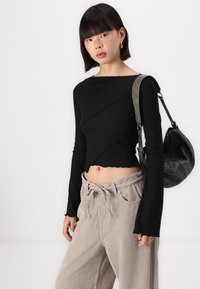Haut noir à manches longues côtelé avec des détails de couture diagonale texturée ; coupe cropped, ourlet festonné. Associé à un pantalon en velours côtelé beige taille haute.