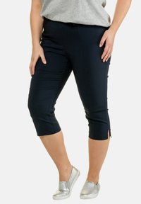 Marineblauwe capri-broeken gemaakt van een gladde stof, met zijsplitten aan de zoom en een aangesloten ontwerp, gecombineerd met zilveren instap-schoenen.