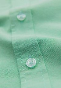 Camicetta a maniche corte in cotone verde menta con un motivo testurizzato, dotata di un bottone trasparente e cuciture abbinate lungo la patta.