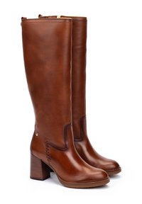 Une paire de bottes en cuir marron, hautes, à talons, avec des bouts ronds, des détails de couture sur les côtés, et des talons blocs sur un fond blanc.