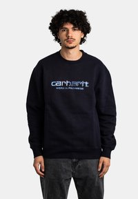 Sudadera azul marino de algodón, con puños y dobladillo acanalados, y logo bordado "carhartt WORK IN PROGRESS" en la parte frontal.