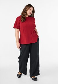 Czerwony top z krótkim rękawem i okrągłym dekoltem, z dyskretnym przeszyciem, w połączeniu z czarnymi spodniami palazzo i czarnymi balerinkami z dekoracyjnymi akcentami.