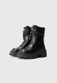 Bottines noires en cuir avec une semelle en caoutchouc épaisse, des zippers en argent et des détails de couture contrastés. Fini lisse, design moderne.