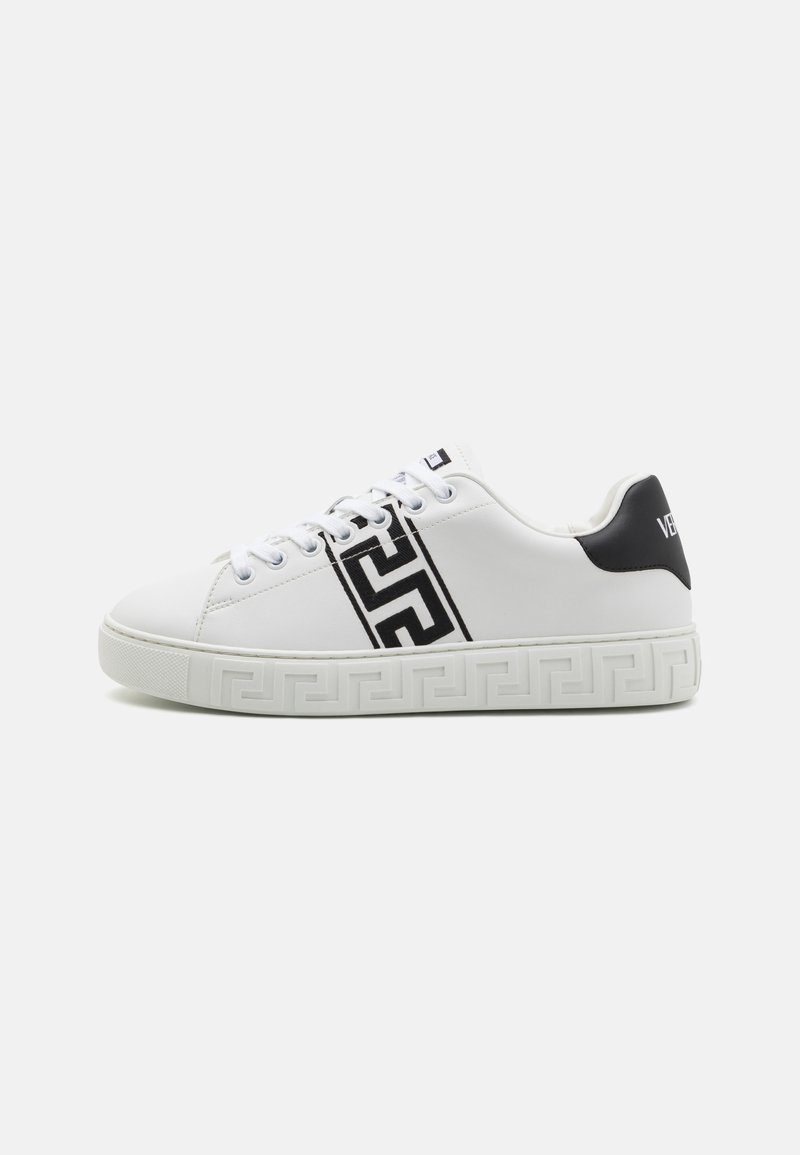 White leather sneakers with a black patterned stripe and black heel accent. Sole features a textured geometric design. Six eyelets for laces.