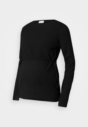 Melnas garām piedurknēm grūtniecības blūze, izgatavota no teksturēta auduma. Tam ir saspiesta josta un sānu saišu, kas nodrošina regulējamu piegulšanu.