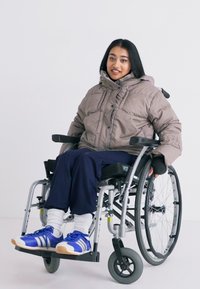 Wheelchair with a gray padded jacket, navy pants, and blue sneakers. The wheelchair features silver metal frame and black wheels.
