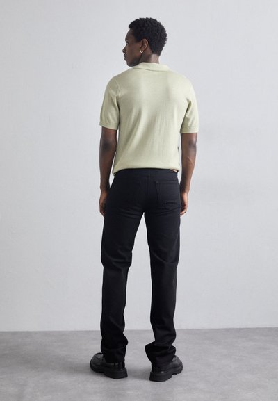 Kortärmad ljusgrön polo skjorta i kombination med svarta jeans, med rak passform och stadiga svarta skor, allt mot en neutral bakgrund.
