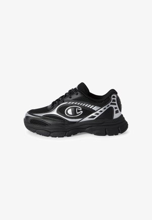 Zapatilla deportiva negra y plateada con tejido de malla, suela gruesa, cordones y un gran logotipo estilizado "C" en el lateral.