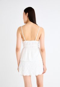 White sleeveless top with a smocked bodice and flared hem, paired with a lace-trimmed white mini skirt, both featuring a textured fabric.