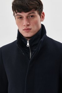 Tamsiai mėlynas vilnos mišinio paltas su aukštu apykakle, turintis užtrauktuką ir subtilius siūlus, struktūruotas siluetas ir lygus paviršius.