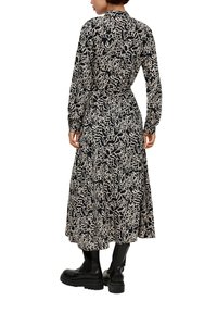 Langes schwarzes Kleid mit beigem abstraktem Muster, langen Ärmeln, tailliert und mit fließendem Rock. Kombiniert mit schwarzen klobigen Knöchelstiefeln.