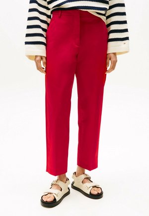 Personne portant un pantalon rouge coupé, un haut rayé noir et blanc à manches longues, et des sandales beiges à bout ouvert avec des semelles noires.
