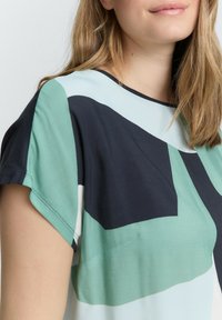 Korte mouwen blouse van zacht materiaal met een geometrisch patroon in donkergroen, lichtblauw en zwart, met een ronde halslijn en een comfortabele pasvorm.