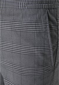 Šedé a černé kostkované kalhoty s texturovanou tkaninou, které mají jemný vzor houndstooth a postranní kapsy.