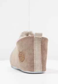 Beige suedestøvlett med myk pelskant, flat såle og et dekorativt logo-patch på hælen. Har en subtil søm langs kanten.