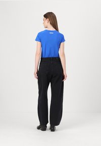 Camicia blu a maniche corte con logo "BOSS" sulla parte posteriore, abbinata a jeans neri a vita alta e a gamba larga e scarpe col tacco nere.