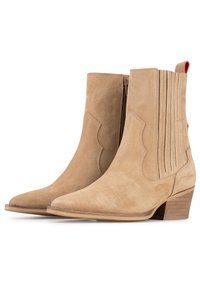 Botas de tobillo de ante beige con puntera afilada, que presentan detalles de costura vertical y un pequeño tacón de madera. Con lengüeta en la parte posterior para ponerlas fácilmente.