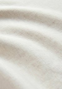 Baumwollstoff in einem elfenbeinfarbenen Farbton mit feinem, strukturiertem Gewebe und glatter, weicher Oberfläche, die sanfte Falten und leichte Variationen zeigt.