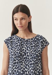 Mieganti pala be rankovių iš lengvos medžiagos, kuri turi tamsiai mėlyną ir baltą leopardų raštą, su suapvalintu iškirpimu ir laisvu siluetu.