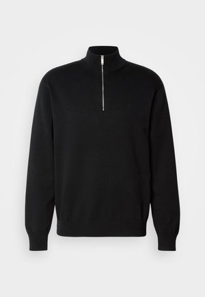 Svart zip-neck genser laget av glatt stoff, med høy krage og lange ermer, samt en subtil logo på brystet.