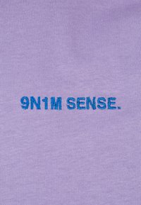 Lilac cotton fabric featuring the embroidered text "9N1M SENSE." in bold teal. The design is simple with a smooth texture.