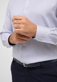 Lichtblauw geblokt shirt met kleine vierkantjes, lange mouwen, knoopmanchetten en beige knopen. Gecombineerd met donkere broeken en eenmarineblauwe riem.