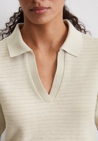 Gebreide pullover in lichtbeige met een V-hals en polo kraag. Heeft een textuurpatroon met horizontale strepen en een zachte, ademende stof.