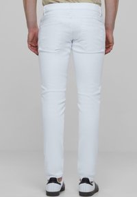 Jeans albe, slim-fit, din denim, cu buzunare pe spate și o textură netedă. Purtați cu adidași negri și albi.