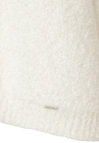 Pull blanc duveteux avec un tissu texturé et doux, et un ourlet côtelé. Une petite étiquette logo argentée est fixée en bas.