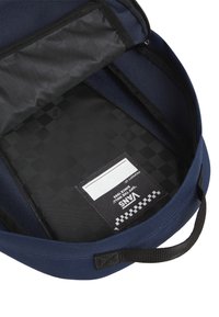 Námořnický modrý batoh s texturovaným vnějším povrchem, černobílou kostkovanou podšívkou a kapsou na štítek uvnitř.