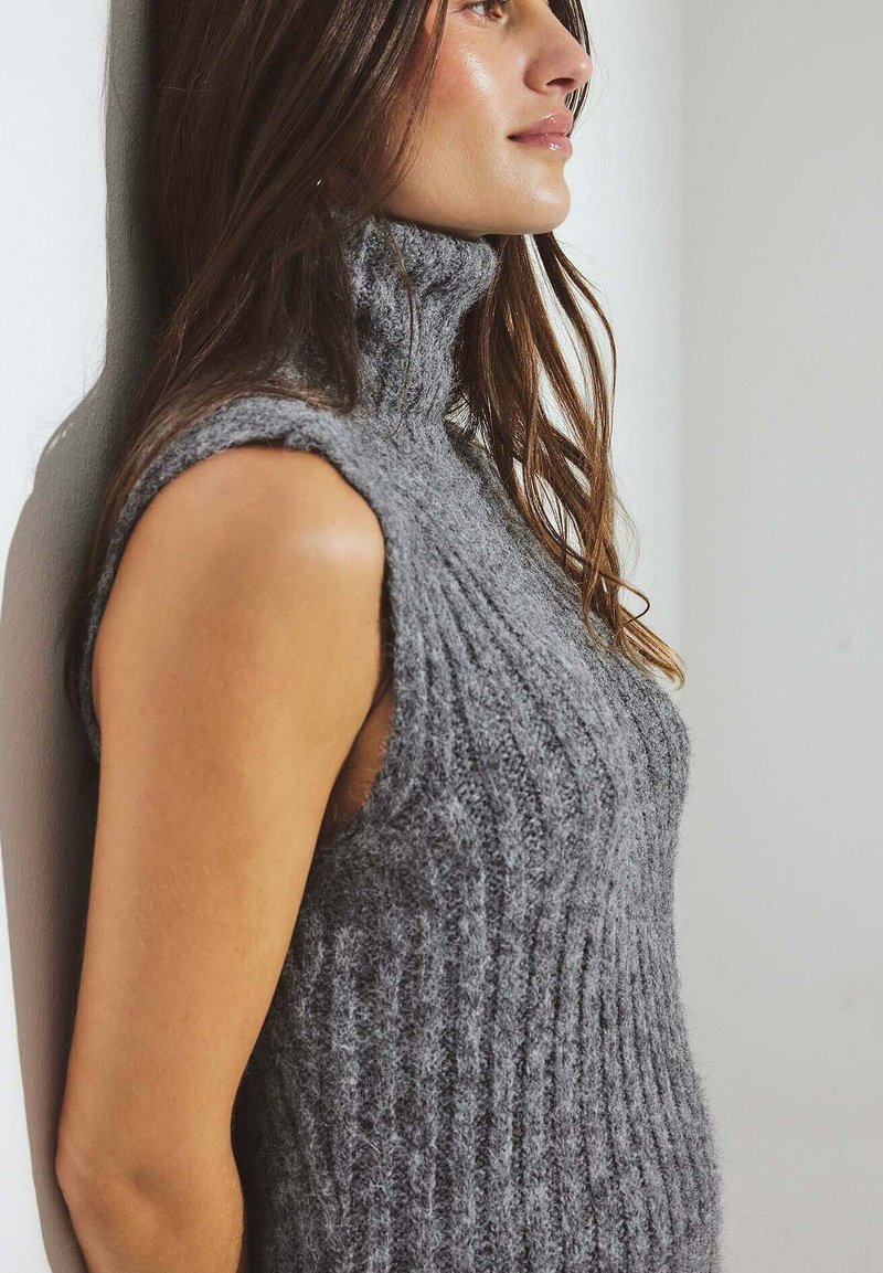 Maglione senza maniche grigio a collo alto in maglia, con texture a coste verticali e finitura morbida, caratterizzato da un design aderente e colletto arrotolato.