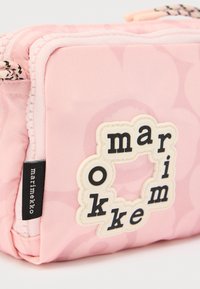 Ροζ υφασμάτινη θήκη με εμπριμέ επιφάνεια, μαύρο και λευκό φερμουάρ και λευκό ταμπελάκι που αναγράφει "marimekko" με μαύρα γράμματα.